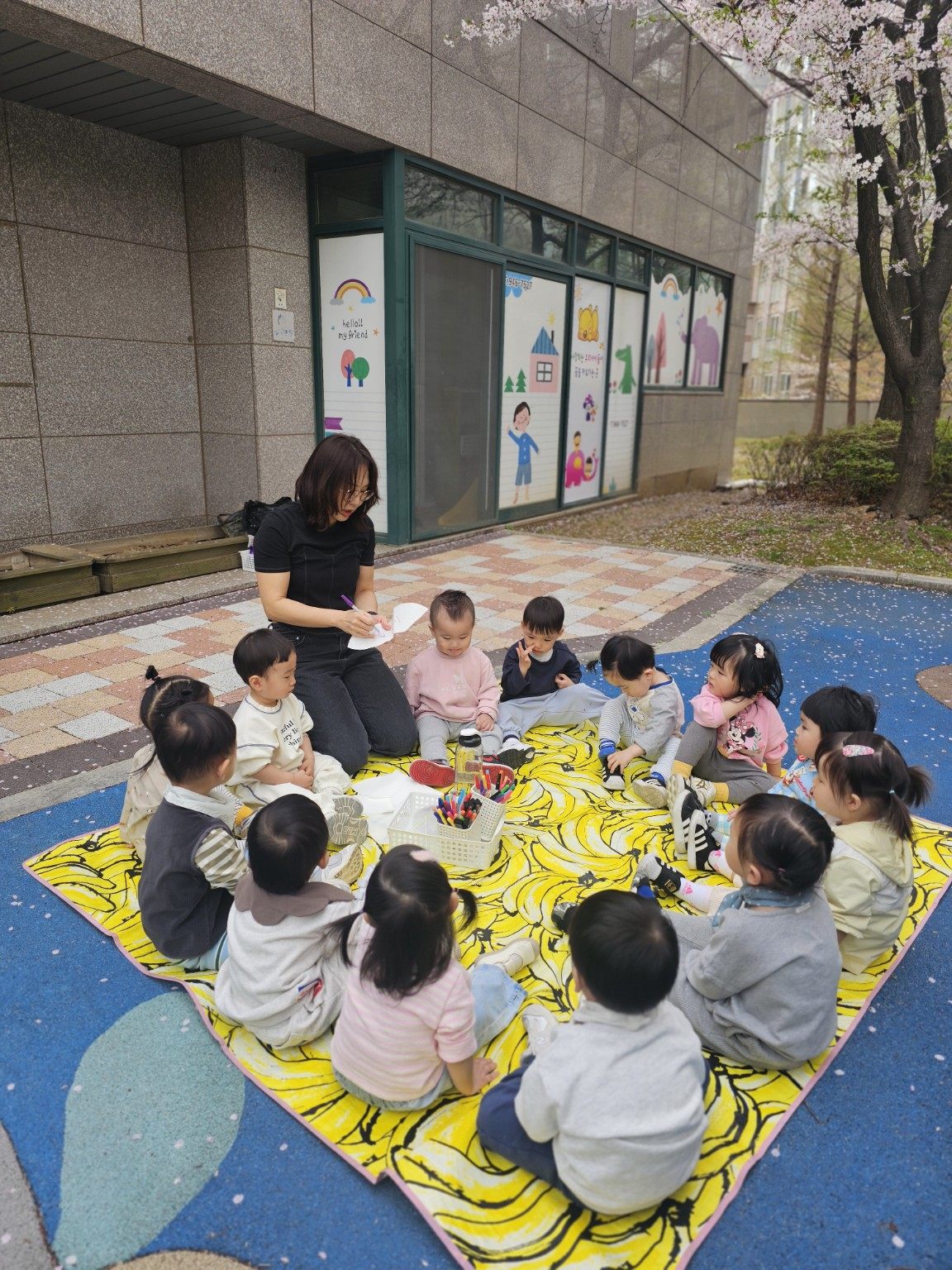 벚꽃 아래 돗자리에 둘러앉아 그림을 그리는 아이들